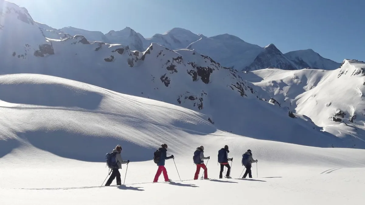 Groupe de cinq randonneurs en raquettes traversant un plateau enneigé face à la chaîne du Mont-Blanc