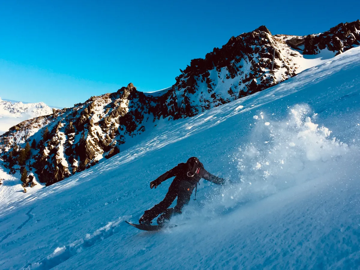 Snowboardeur en pleine courbe dans la poudreuse, au-dessus de la vallée de Chamonix